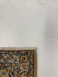 Close-up corner of a patterned area rug with cream, navy, orange, and beige floral motifs, shown against a white textured wall.