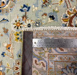 Close-up of a patterned area rug with a floral design in muted blue, beige, brown, and cream tones, shown with a metal ruler to indicate scale.