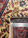 Close-up of a patterned rug with cream, red, blue, and green floral motifs, showing the fringe edge and a stainless steel ruler for scale.