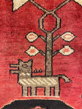 Close-up of a woven rug or textile with a red field, a central beige and brown geometric motif, and small cream and pink floral shapes.