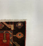 A close-up corner view of a patterned rug with cream fringe, shown against a white surface and gray carpet background.