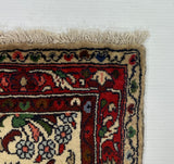 A white rectangular board or panel placed on a gray carpet, with the corner of a patterned rug visible in the lower right. The rug has cream, red, blue, and green detailing with a fringed edge.