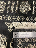 Close-up of a black and cream patterned rug with a visible woven fringe and a stainless steel ruler placed vertically to show scale.