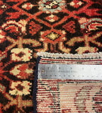Close-up of a patterned textile or rug showing a dark brown and red geometric design with cream accents, plus a metal ruler placed along the edge to indicate scale.