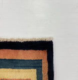 A close-up of a multicolor patterned rug corner laid next to a large white board on a gray carpeted floor.