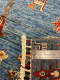 Close-up of a blue patterned rug with cream fringe and a stainless steel ruler placed on the woven edge to show texture and scale.